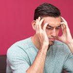 Closeup portrait of tensed young man thinking hard and touching head with fingers at home